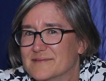 Person wearing glasses and a black-and-white patterned shirt against a dark blue background.