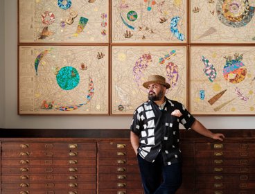 Artist Hormazd Narwiella stood in front of map drawers and modern art.