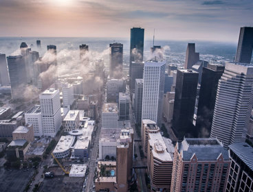 Drone view of city skyscrapers with low clouds between the buildings.
