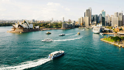 A skyline view of Sydney, Australia, as seen from the sea, showing boats and the Sydney Opera House.