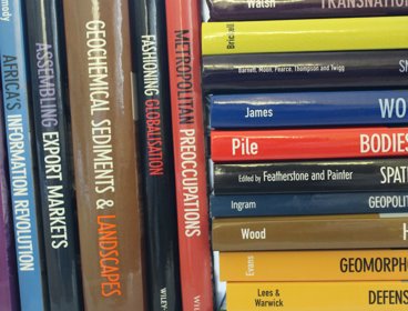 Two stacks of geographical journals. On the left the books are stacked vertically and on the right the books are stacked horizontally.