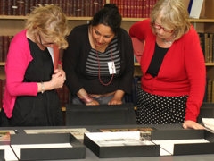 Three people looking at archived Collection item in a library.