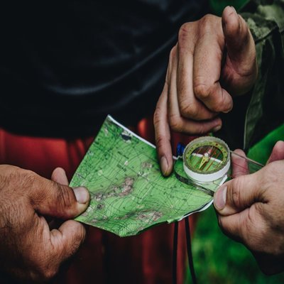 Hands holding a small map and compass. The map is mainly green and you can see contour lines on it