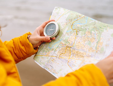Close up of a person in a bright yellow coat holding a map and a compass.