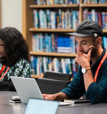 Two people using laptops while seated at a table in a library.