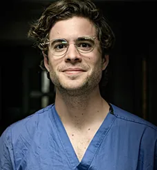 Jon Williamson in scrubs with all-black background.