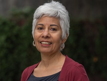 Portrait of a person in a red cardigan with short hair and hoop earrings.