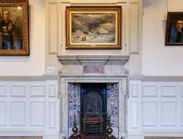 Wall in historic room featuring a fireplace and oil paintings hanging on the walls.