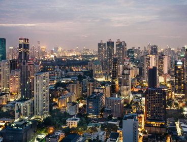 A cityscape at dusk with modern high rise buildings and lit up streets.