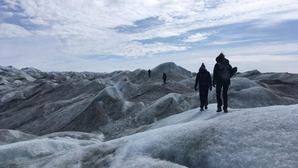 Four people walking across an undulating glacial landscape carrying equipment.