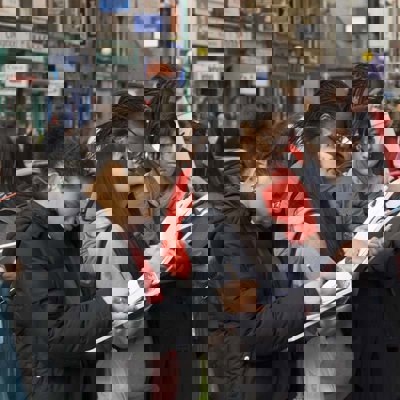 A group of female school children, holding clipboards and looking at buildings on a high street