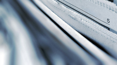 A selective focus photograph of the top corner of a stack of newspapers.