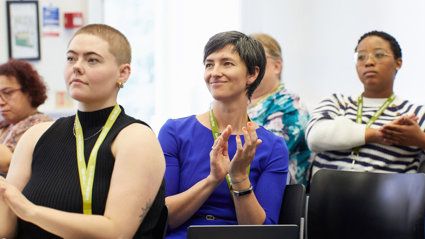 Three conference delegates listening to a presentation and apploading.