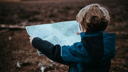 A young child in the outdoors holding a map.