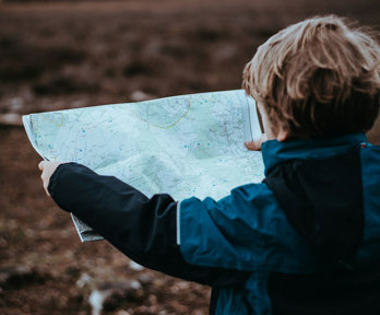 A young child in the outdoors holding a map.