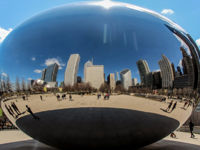 A huge silver coffee bean shaped structure in Chicago, which reflects the city skyline and blue skies