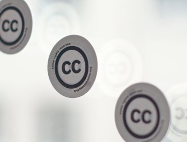 Three stickers with the creative commons logo on a window.