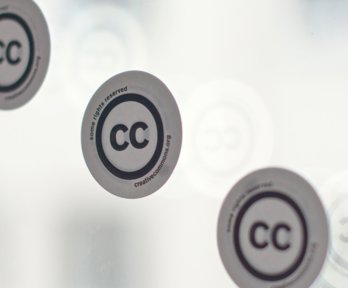 Three stickers with the creative commons logo on a window.