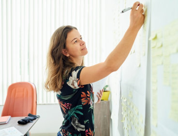 Person writing on a post-it note stuck on a wall.