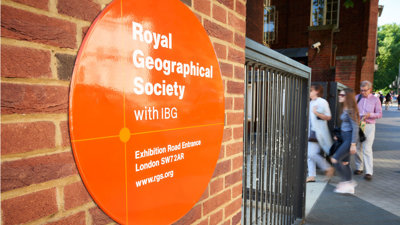 Sign on the outside of the Society's building close to the entrance, with three people walking in.