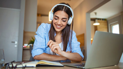 Person wearing headphones smiles while studying with a notebook and laptop.