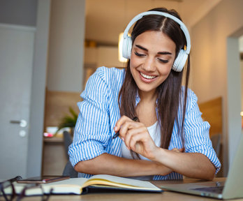 Person wearing headphones smiles while studying with a notebook and laptop.