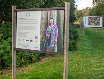Wooden sign in a field of grass with a text about the Earth Photo 2023 exibition on the left and one of the winning images to the right.