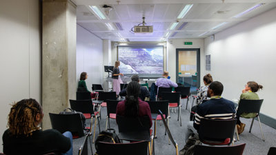 Several people sit in a room facing a presenter.