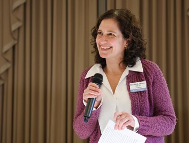 Person in a purple cardigan speaking into a microphone.