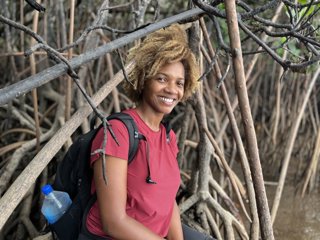 Person in red t-shirt and wearing a backpack sitting at the edge of mangroves.