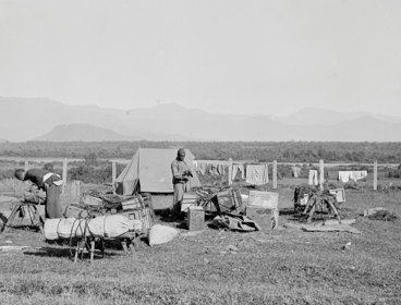 Four people camping in a vast field, in Fort Hertz, North Burma. Mountains can be seen far in the background. This visual is not in colour.