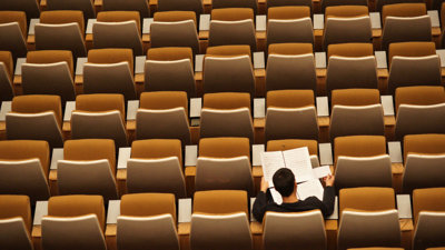 Person sits alone in a lecture hall whist reading through several papers.