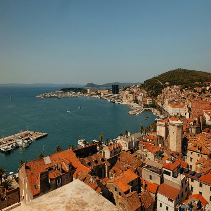 A view over a Mediterranean town by the sea. The roofs are orange tile and several jettys for boats can be seen