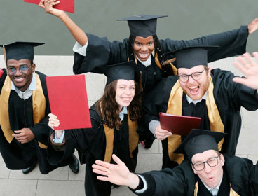 Group of five people in graduation gowns celebrating and raising their certificates.