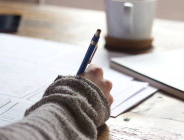 Close up of a person writing at a desk.
