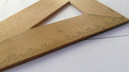Close up of a brown wooden measuring tool laying on a sheet of paper.