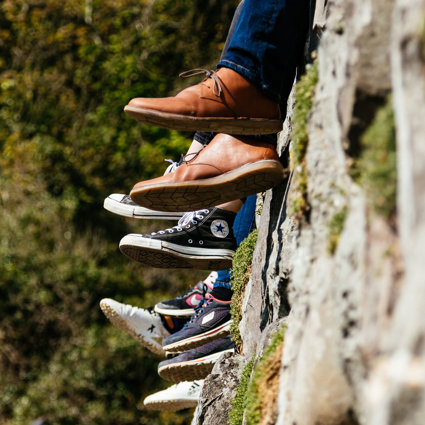 A group of people sitting on a wall but you can only see their feet dangling over the side.