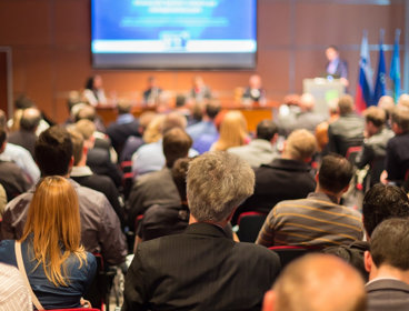 People sat at a conference in the audience as seen from behind.