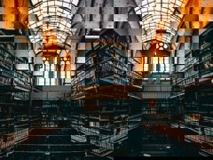 A dark, historic library with towering shelves and an arched glass ceiling.