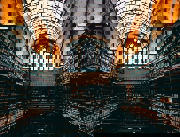 A dark, historic library with towering shelves and an arched glass ceiling.