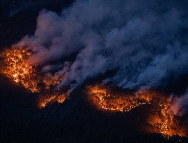 Wildfire at night with large plumes of smoke as seen from above.