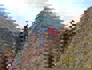 Two researchers sit on a sloping valley side while one stands, facing the others. They are all writing in notebooks.