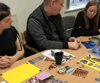 A group of people sitting at a table with pieces of artwork and craft supplies