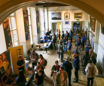 A large gathering of people networking in a stately main hall, as seen from above.