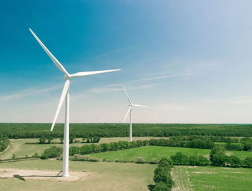 Two wind turbines in open fields with a clear sky.