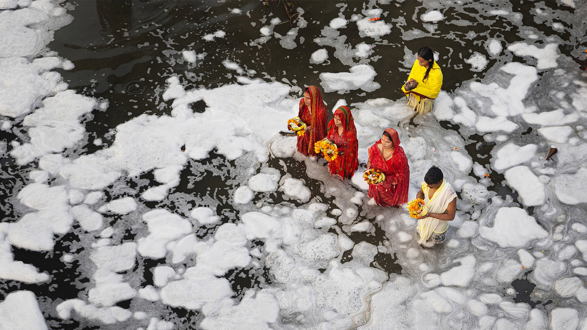 A group of people wearing traditional Indian clothing standing in a river while performing a religious ritual.