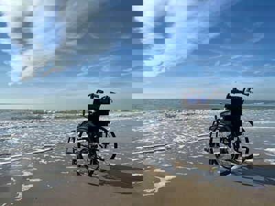 An empty wheelerchair on a sandy beach, facing towards the sea