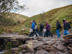 Group of people doing fieldwork. They are walking across rocks in a mountainous region.