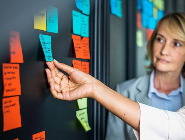 Colleagues placing colourful sticky notes on a glass board.