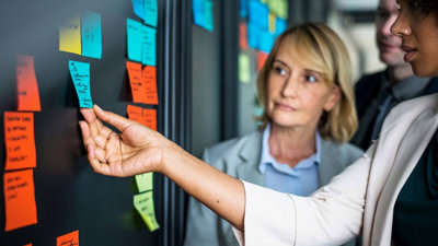 Colleagues placing colourful sticky notes on a glass board.